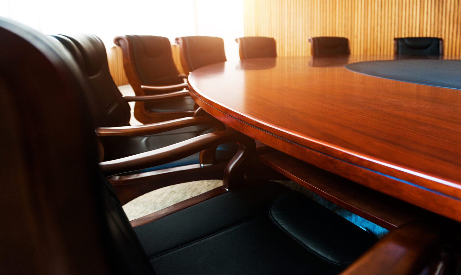 The well-lit room features a large oval wooden conference table surrounded by black leather chairs, creating an ideal setting for discussions or hosting court reporting services.